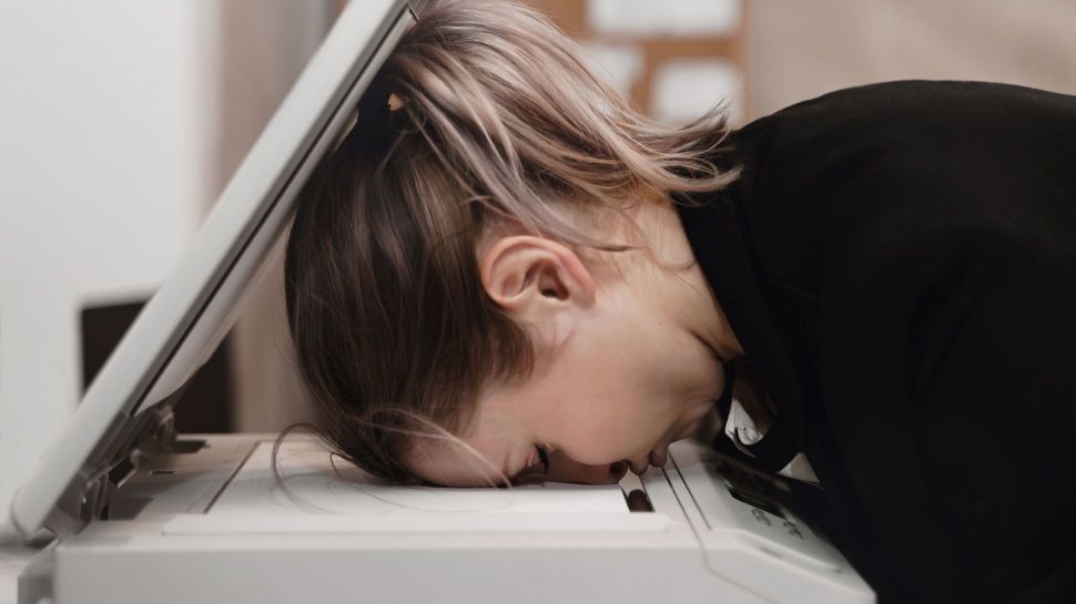 Person resting their head in despair on a printer
