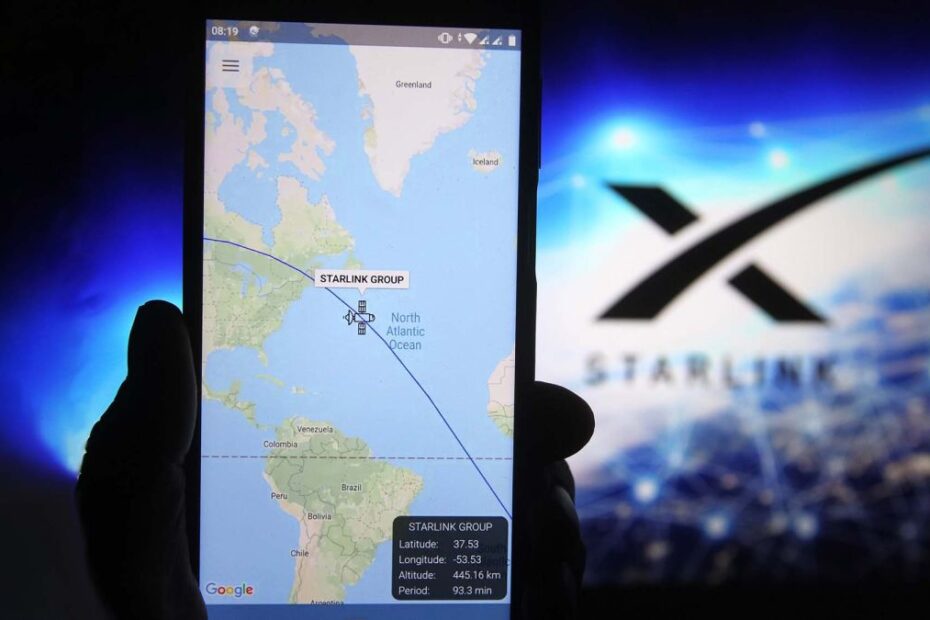 A satellite tracker image is seen displayed on a smartphone with a Starlink logo in the background