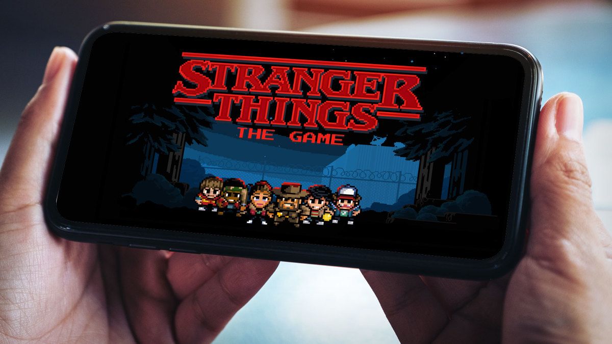 An image of a person holding a mobile phone in landscape mode with the Stranger Things: The Game title screen loaded up