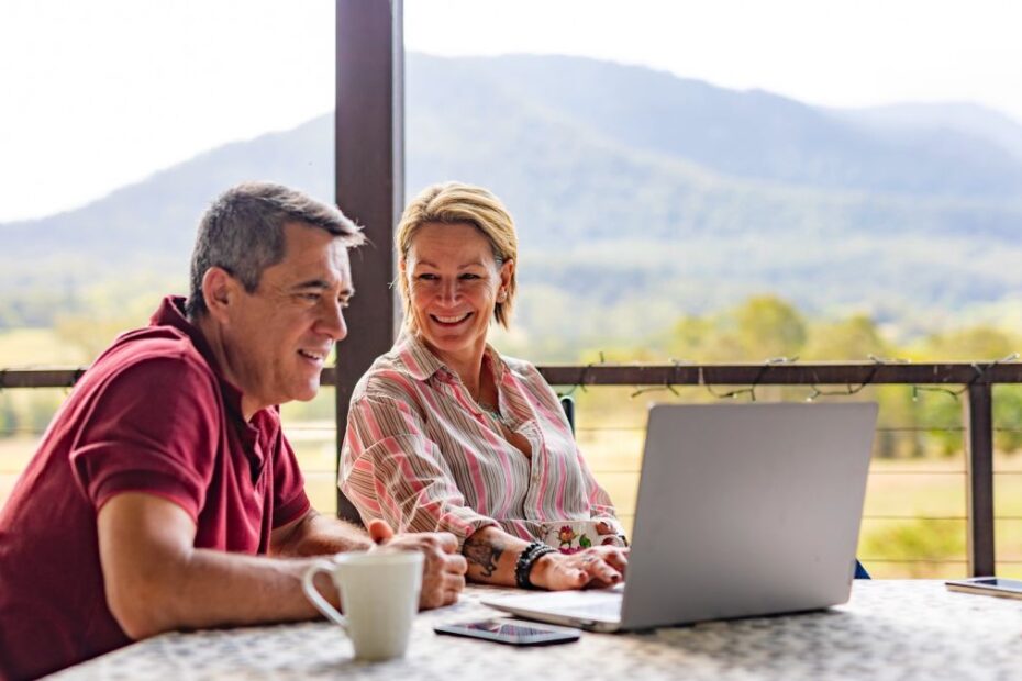 A middle-aged couple using a laptop on the verandah of their farm in rural Australia
